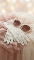 Elegant white lace gloves and pearl-adorned sunglasses on soft pink tulle fabric with dreamy bokeh lights for luxury fashion and bridal styling.