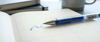 Blue ballpoint pen with ink mark on open notebook page, suitable for writing, education, office work, and stationery design projects.