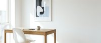 Minimalist home office with wooden desk, white chair, mug, and abstract wall art in a bright, airy Scandinavian-style room.