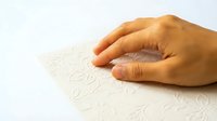 Hand reading braille text on white paper, tactile learning system for visually impaired education and accessibility communication support.