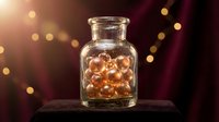 Glass jar filled with golden amber spheres on dark surface with warm bokeh lights and burgundy background, suitable for wellness, skincare, supplement, and luxury product packaging designs.