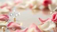 Soft pink and white rose petals scattered with sparkling pearls on light background for romantic wedding or Valentine's Day celebration designs.