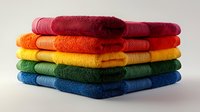 Stack of folded rainbow colored cotton bath towels arranged in spectrum order from red to blue, photographed against neutral background showing texture and layers.