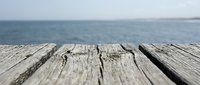 Weathered wooden pier deck with ocean and horizon in soft focus background, suitable for travel and nature themes.