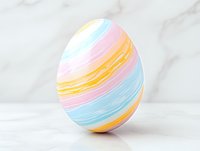Decorative Easter egg painted in soft pastel stripes of pink, blue and yellow on white marble background, modern minimalist spring holiday design.