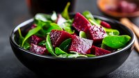 Fresh beetroot salad with baby spinach leaves in black ceramic bowl on dark background, healthy vegetarian meal with vibrant colors and natural ingredients.