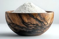 White flour in rustic wooden bowl with distinctive dark grain pattern against light background, showcasing natural texture and artisanal baking ingredients.
