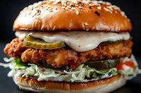 Crispy chicken sandwich with melted cheese, pickles and shredded lettuce on sesame seed bun, close up view against dark background for menu and food advertising.