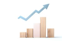 Wooden blocks arranged as bar chart with light blue arrow trending upward, showing business growth and success concept on white background.