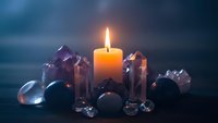 Burning candle surrounded by healing crystals and gemstones creating mystical atmosphere for meditation, spirituality and wellness practices.