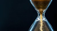 Time running out concept with golden sand flowing through hourglass against dark background for business deadlines and urgency themes.