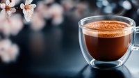 Hot coffee in glass cup with spring blossoms and cocoa powder on dark surface. Perfect for beverage, café, and seasonal marketing materials.