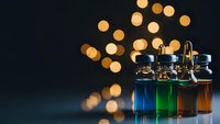 Laboratory glass vials with colorful liquids and golden bokeh lights on dark background for scientific research and chemistry experiments.