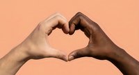 Two diverse hands forming heart shape symbol representing unity love and racial harmony against coral background for social campaigns.