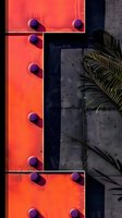 Modern industrial wall with orange metal panel, purple rivets casting shadows, and palm leaf creating contrast. Architectural detail for urban design backgrounds.