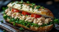 Fresh tuna salad sandwich on artisanal bread garnished with crisp lettuce, juicy tomatoes and herbs, macro food photography on dark background.