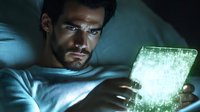 Man with intense gaze holding glowing futuristic transparent tablet device in dark room, illuminated by cyan digital screen light creating dramatic atmosphere.