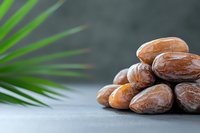 Fresh dates fruit pile on gray surface with green palm leaf, healthy organic snack food for Mediterranean diet and natural nutrition lifestyle.