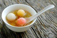 Traditional Asian dessert soup with colorful glutinous rice balls in sweet broth served in white bowl with spoon on bamboo mat for cultural cuisine.