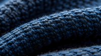 Close up macro shot of dark blue knitted wool fabric texture showing detailed pattern of yarn threads and stitches in soft lighting.