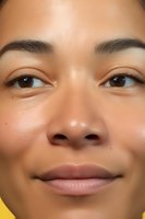 Close-up portrait of young Asian woman with natural makeup and glowing skin showing genuine smile against yellow background, focus on eyes and lips.