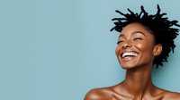 Young African American woman with natural hair laughing joyfully against blue background, expressing genuine happiness and positive emotions in studio portrait.