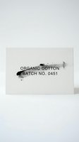Minimalist organic cotton product label with black ink brush strokes on textured paper background for natural skincare and eco-friendly branding design.