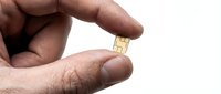 Closeup of male hand holding small gold microchip or SIM card isolated on white background for technology and electronics concepts.