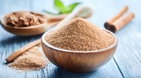 Brown sugar in wooden bowl with cinnamon sticks on rustic blue table. Natural sweetener and spice ingredients for baking and cooking. Close up view with soft focus.