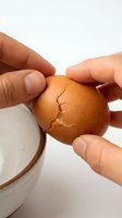 Hands cracking a fresh brown egg over a ceramic bowl on a white background, close-up cooking preparation concept.