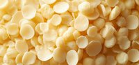 White chocolate callets in round disk form scattered across surface, macro food photography showing texture and glossy finish of confectionery ingredients.
