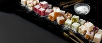 Assorted colorful Turkish delight lokum sweets arranged on dark slate board with powdered sugar for gourmet dessert and confectionery presentations.