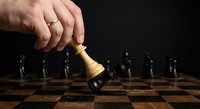 Male hand moving golden king chess piece on wooden chessboard against dark background, strategic business planning and leadership concept for corporate success.