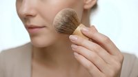 Woman applying powder with makeup brush to cheek for cosmetic beauty routine and skincare application.