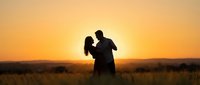 Romantic couple silhouette embracing at golden sunset in open field, warm orange sky creating intimate moment for wedding, love and relationship concepts.