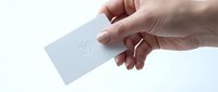 Caucasian hand holding blank white business card with embossed heart symbol, isolated on white background for branding, corporate identity, and stationery design mockups.