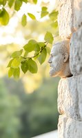 Stone sculpture profile of bearded man emerging from ancient wall with fresh green leaves and soft bokeh background in morning light. Peaceful spiritual atmosphere.