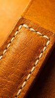 Orange leather material with white decorative stitching detail showing craftsmanship and texture for luxury goods, fashion accessories, and handmade products.