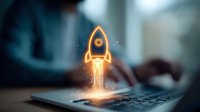 Glowing orange rocket launching from laptop keyboard with sparks and light effects against blurred office background, symbolizing business startup and growth.