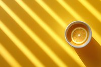 White ceramic cup with fresh lemon slice on golden background with diagonal light and shadow stripes creating minimalist composition and dramatic lighting effect.