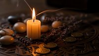 Mystical fortune telling setup with burning candle, ancient coins and runes on ornate wooden table creating atmospheric divination scene for spiritual practices.