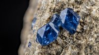 Blue sapphire gemstones embedded in natural rock matrix showing crystalline structure and mineral formation for jewelry and geological study purposes.