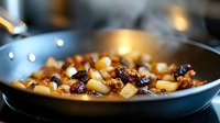 Sautéed diced potatoes with caramelized onions and herbs cooking in stainless steel pan on stovetop for home cooking and culinary preparation recipes.