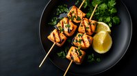 Grilled salmon skewers with fresh herbs and lemon on black plate against dark background. Seafood kebabs garnished with parsley and citrus for restaurant menu.