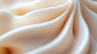Smooth flowing cream-colored satin fabric creates elegant waves and folds with soft shadows and highlights, suitable for luxury fashion and wedding backgrounds.