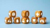 Wooden healthcare dice with medical symbols including brain, DNA, cross, pills, blood drop, tooth and lungs on light blue background for wellness concepts.
