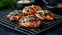 Grilled teriyaki chicken thighs with sesame seeds and green onions on black grill grates, glazed with sweet and savory Asian marinade. Food photography.