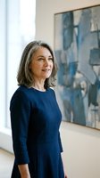 Confident mature businesswoman with gray hair in navy blue dress standing in modern office with abstract art background for corporate leadership concepts.