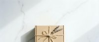 Kraft paper gift box tied with twine and dried wheat stems on white marble surface, overhead view for holiday, celebration, and eco-friendly packaging design projects.