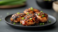 Glazed teriyaki chicken thighs garnished with sesame seeds and green onions served on black plate. Close up view of juicy grilled meat with asian sauce.